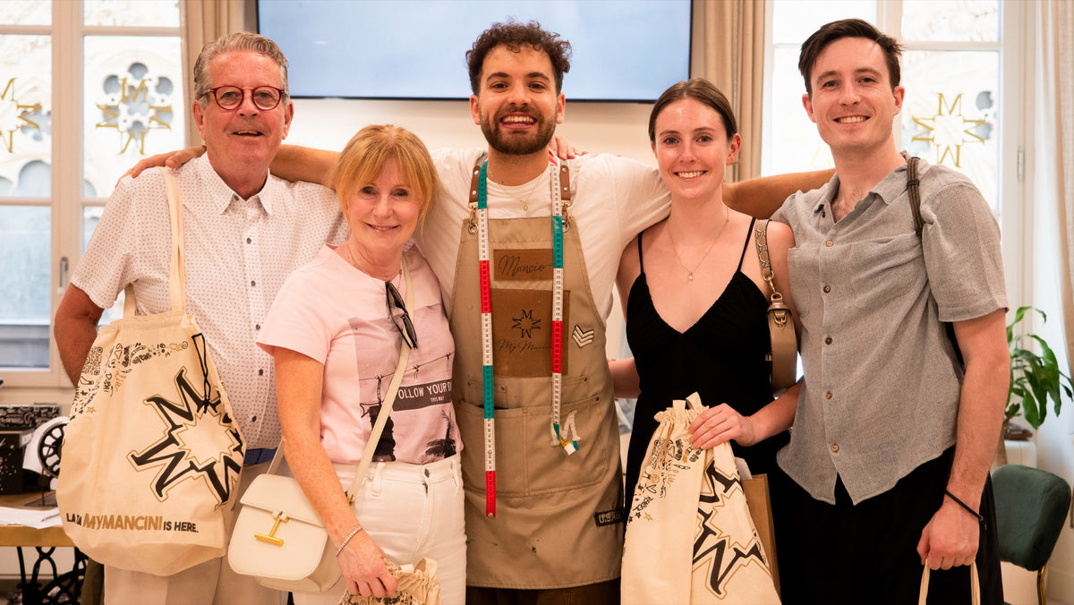 Group of five people posing together in a room with bags.